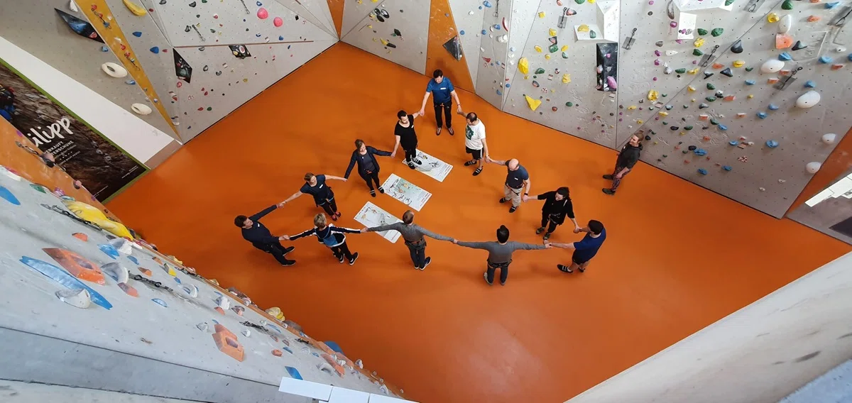 Ein Team steht gemeinsam in der Boulder Halle und hält sich an den Händen.