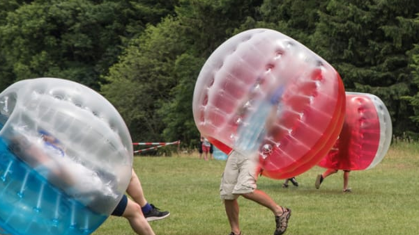 Mehrere Menschen spielen mit einer Bubble Ausrüstung gegeneinander Fußball auf einem Fußballfeld.