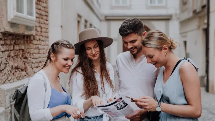 Vier Menschen schauen auf ein Blatt Papier, und lesen, was darauf steht. Eine Person hält ein Handy in der Hand und schaut etwas nach.