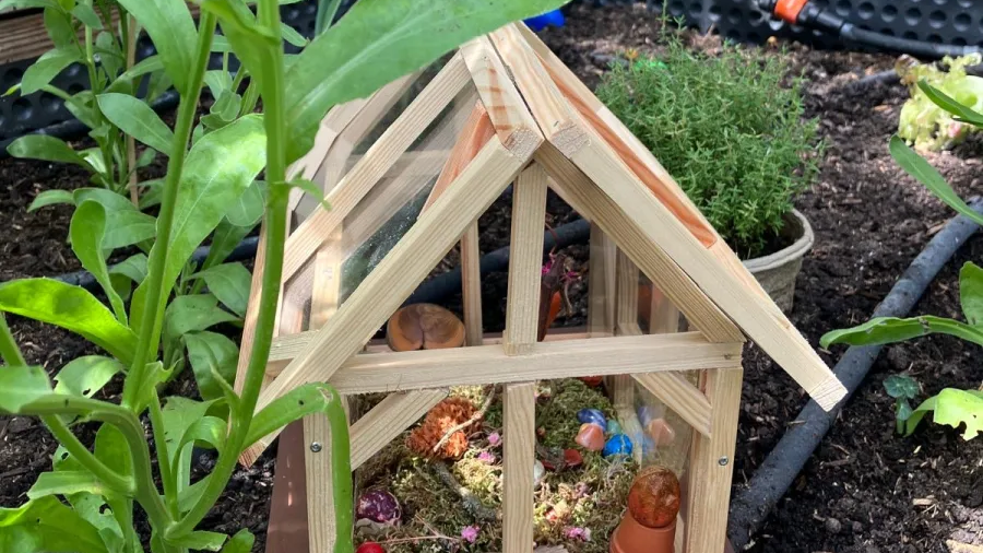 Ein kleines Holzhaus steht in einem Beet. In dem Holzhaus befinden sich Moss und Steine.