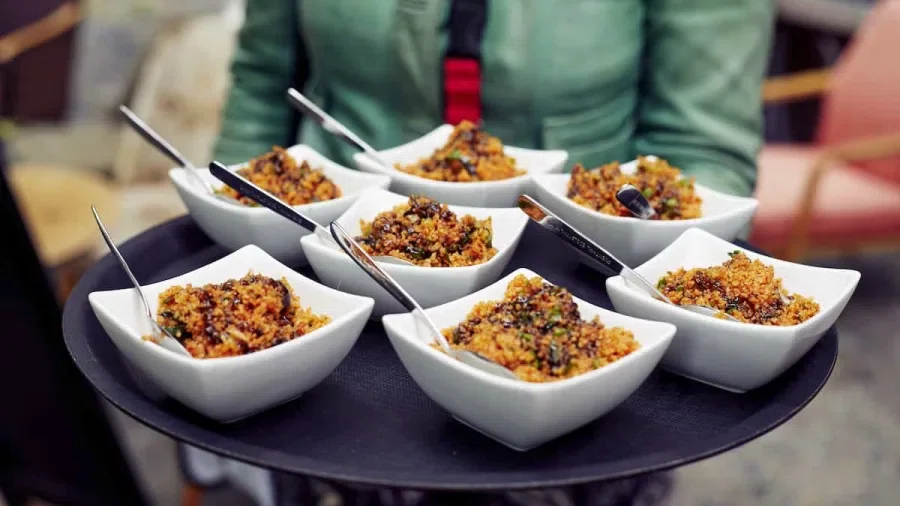 Mehrere kleine Schüsseln mit Essen stehen auf einem Tablett, das von einem Mann gehalten wird.