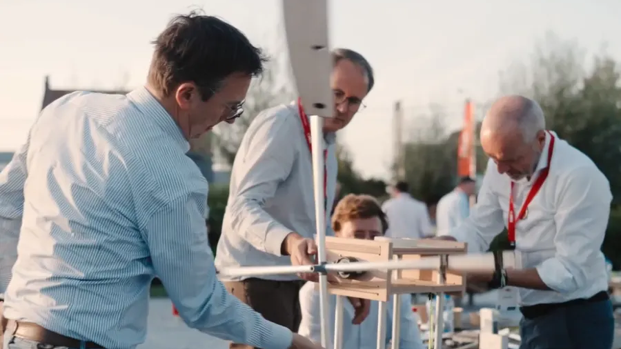 Drei Männer bauen aus Holz ein Windrad zusammen.