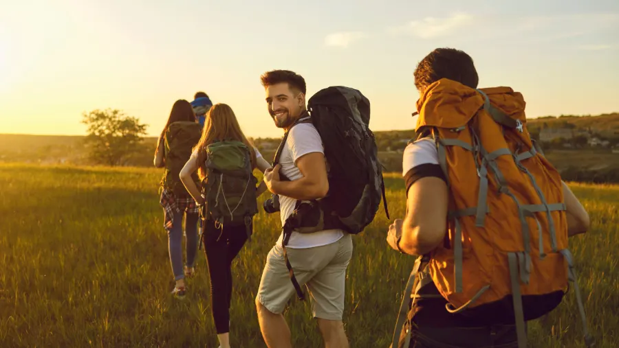Mehrere Menschen laufen hintereinander in einem Feld mit Rucksäcken auf dem Rücken.