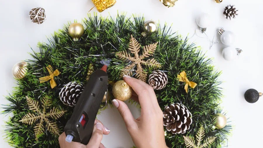 Jemand klebt mit einer Heißklebepistole weihnachtliche Dekoration an einen Adventskranz.