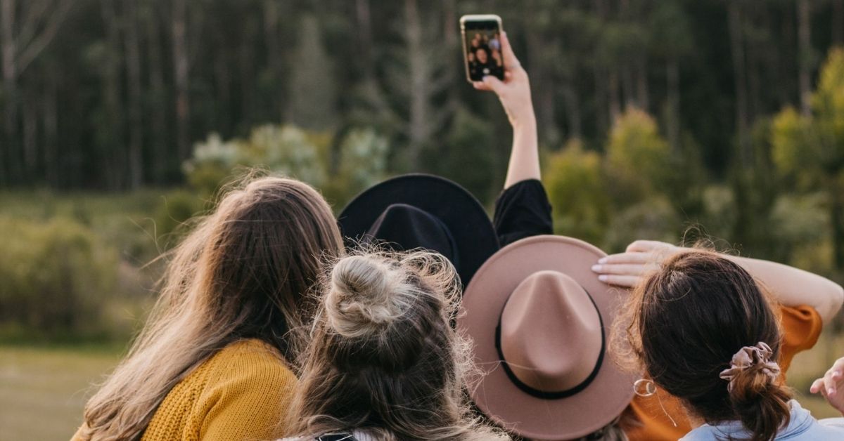 Ein Team steht auf einer Wiese vor dem Wald und macht mit dem Handy ein Selfie von sich.